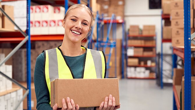 Porträt einer Arbeiterin, die eine Kiste in einem Lagerhaus hält