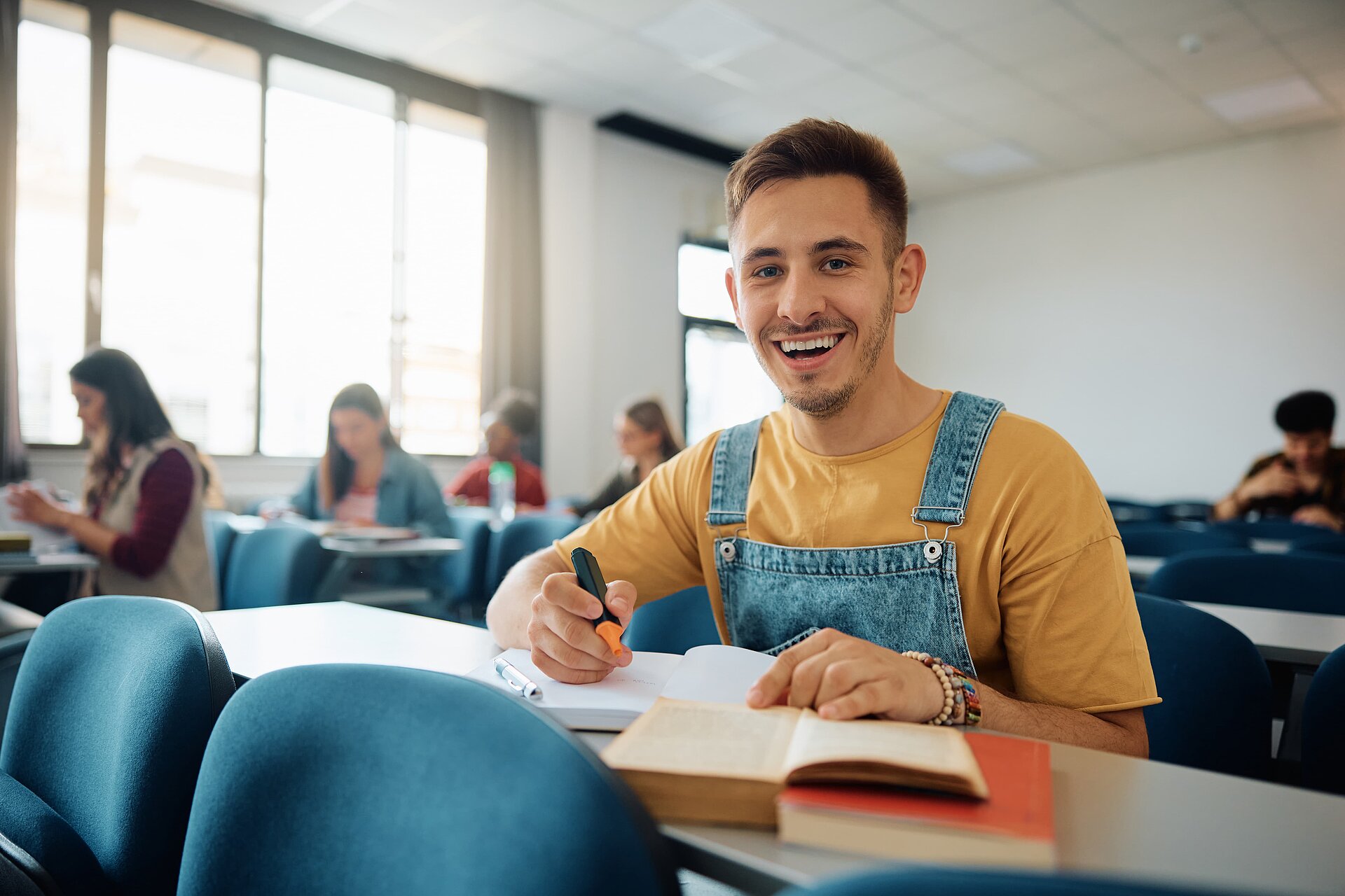 Šťastný student, který se učí v přednáškové síni a dívá se do kamery.