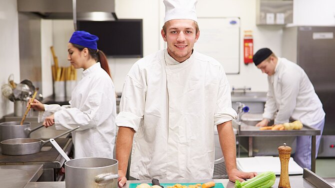 Koch steht in der Küche mit Mitarbeitern im Hintergrund