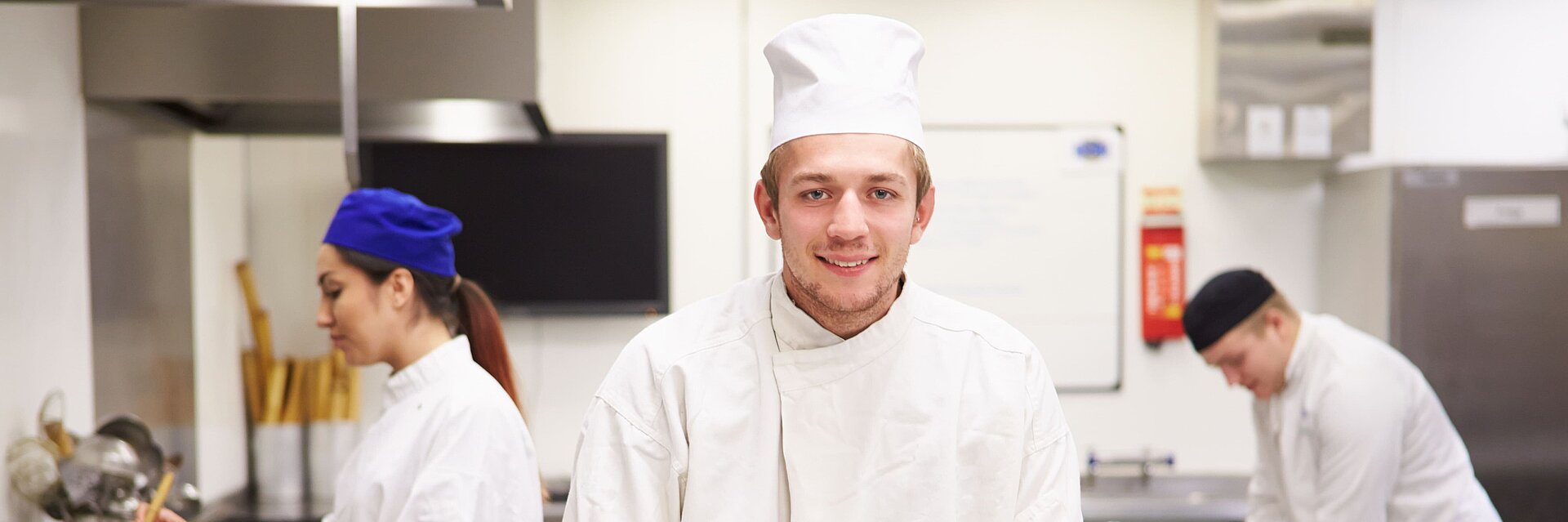 Koch steht in der Küche mit Mitarbeitern im Hintergrund